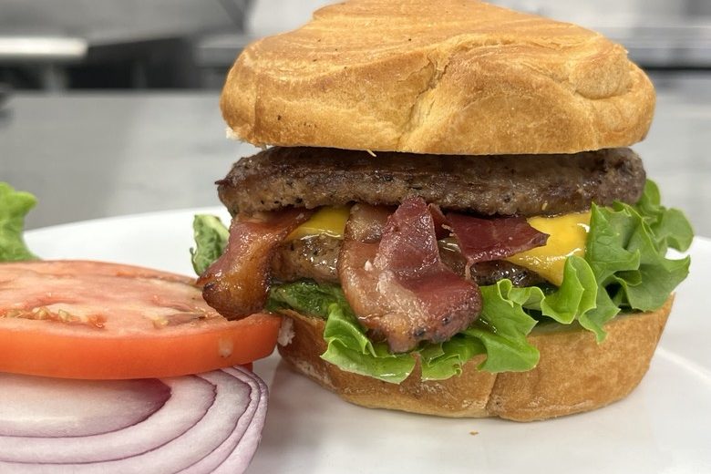 Bacon Burger A bacon cheeseburger topped with lettuce, tomato, and red onion on a toasted bun.