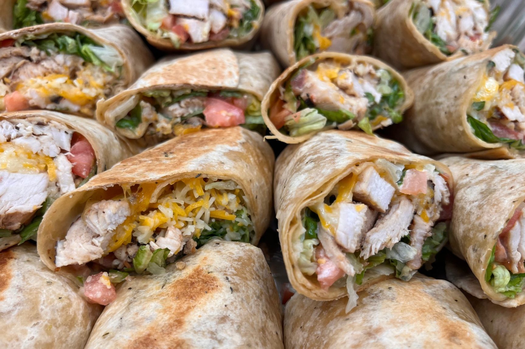 Sandwich Platter A close-up of multiple chicken wraps filled with lettuce, tomatoes, and cheese.